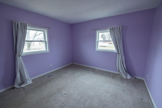 carpeted spare room with visible vents, baseboards, and a textured ceiling