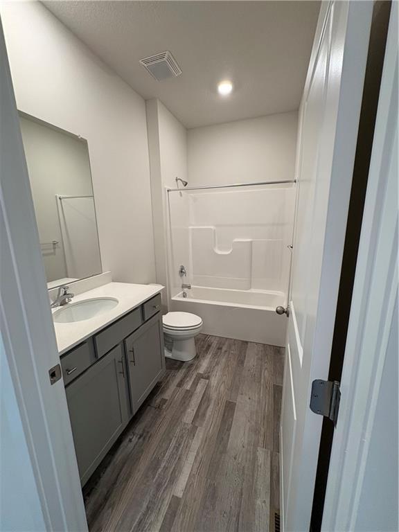 bathroom with visible vents, toilet, shower / bath combination, wood finished floors, and vanity