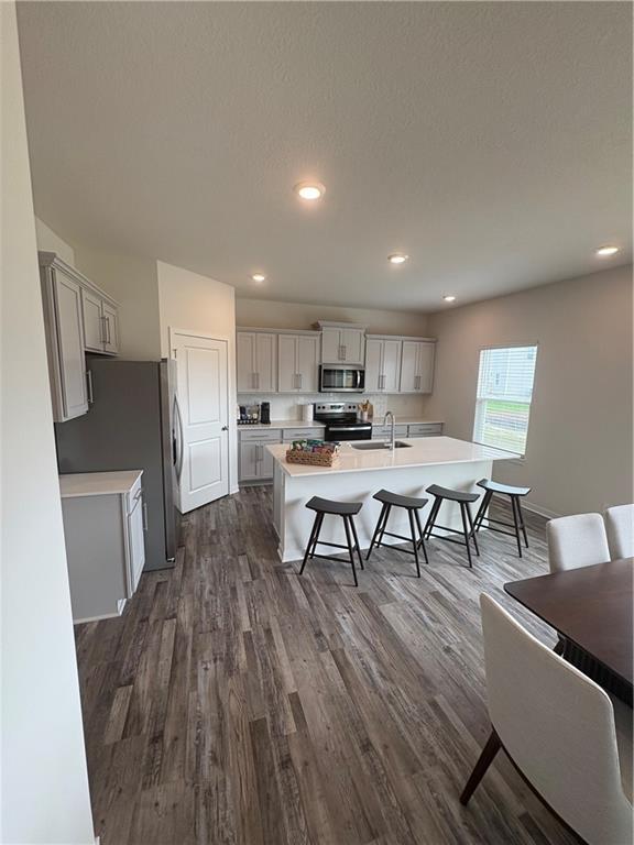 kitchen featuring dark wood-style floors, a sink, a breakfast bar, light countertops, and appliances with stainless steel finishes