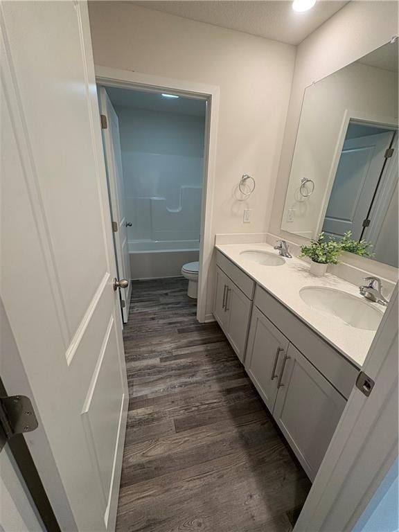 bathroom featuring wood finished floors, toilet, double vanity, and a sink