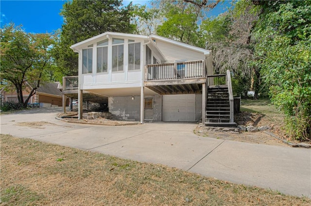 view of front facade with stairway, a wooden deck, concrete driveway, a sunroom, and an attached garage