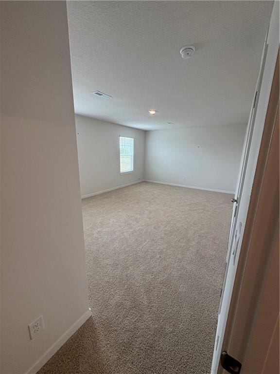 carpeted spare room with baseboards, visible vents, and a textured ceiling