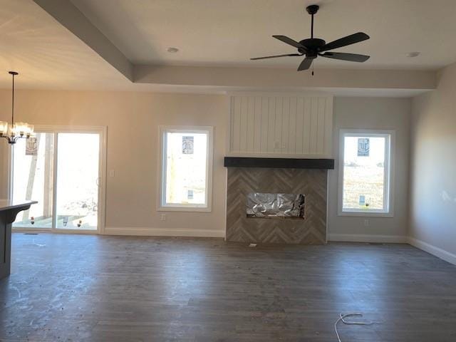 unfurnished living room featuring ceiling fan with notable chandelier, dark wood-type flooring, and baseboards