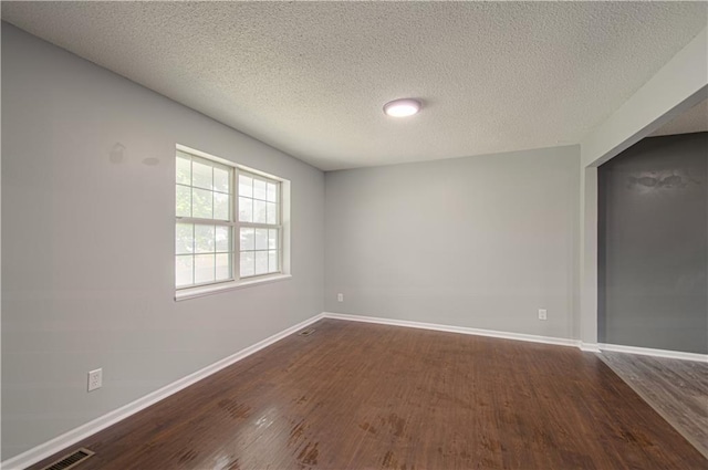 unfurnished room with visible vents, baseboards, a textured ceiling, and dark wood-style flooring