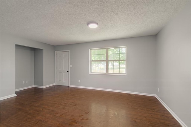 empty room featuring baseboards, dark wood-type flooring, and a textured ceiling