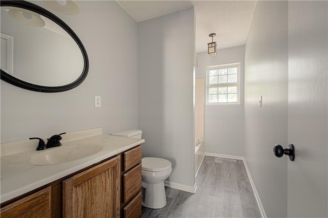 full bathroom featuring toilet, a textured ceiling, wood finished floors, baseboards, and vanity