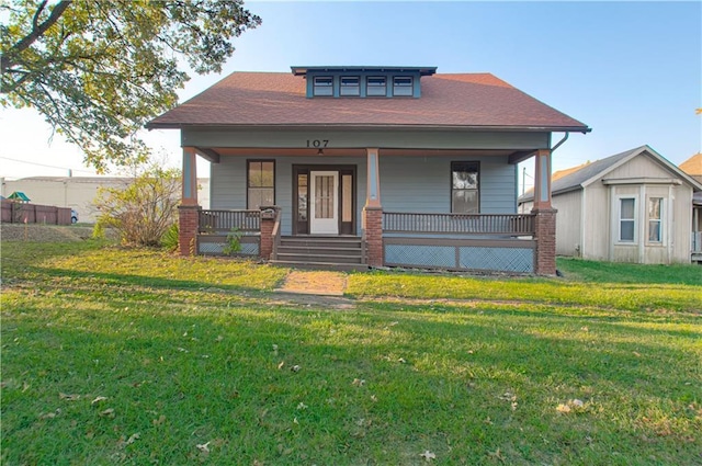 bungalow-style house with covered porch, a front lawn, and a shingled roof