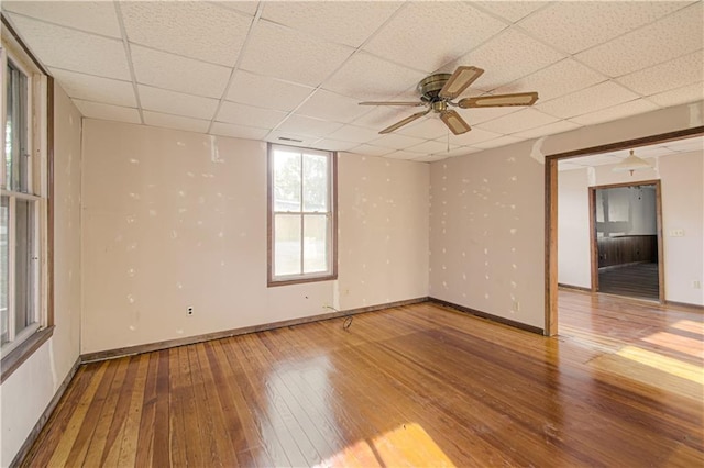 unfurnished room with a paneled ceiling, baseboards, wood-type flooring, and ceiling fan