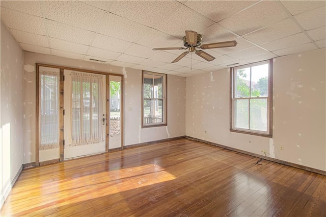 empty room with a drop ceiling, baseboards, ceiling fan, and hardwood / wood-style flooring