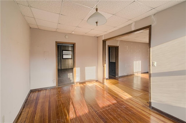 empty room featuring a drop ceiling, baseboards, and hardwood / wood-style flooring