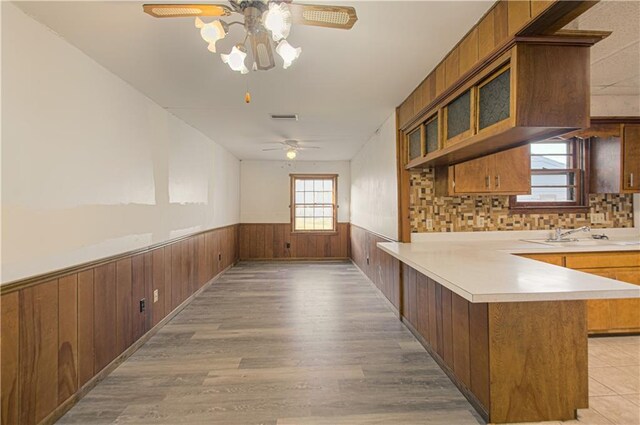 kitchen featuring light countertops, wainscoting, a peninsula, brown cabinetry, and a sink