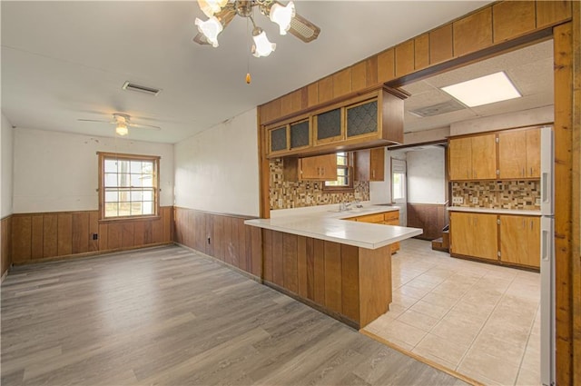 kitchen with brown cabinetry, visible vents, a wainscoted wall, a peninsula, and light countertops