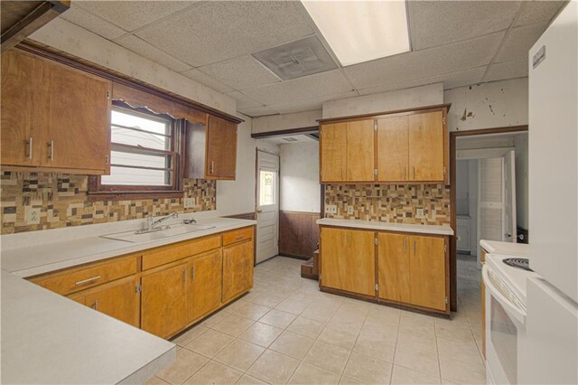 kitchen with brown cabinetry, a drop ceiling, a sink, light countertops, and white electric range