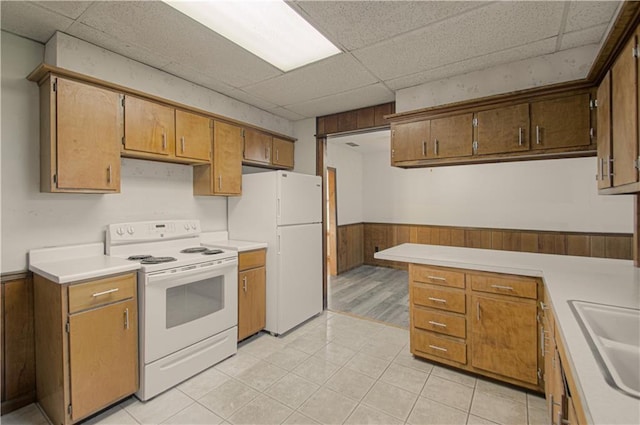 kitchen with white appliances, light countertops, a wainscoted wall, and a paneled ceiling