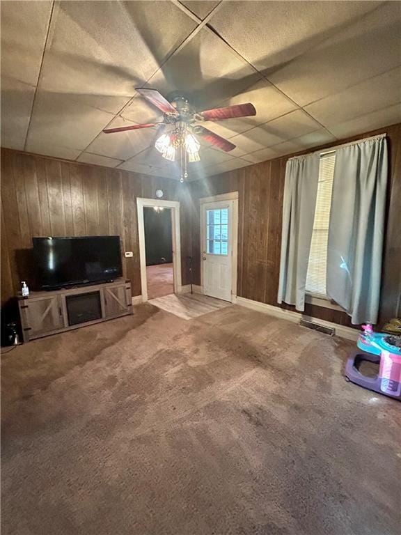 living area with visible vents, a ceiling fan, wood walls, and carpet floors