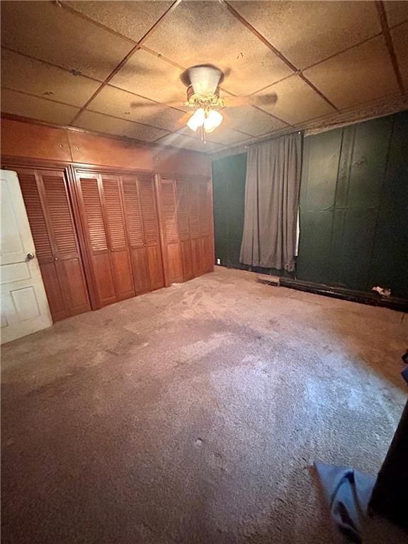 unfurnished bedroom with a ceiling fan, a drop ceiling, and carpet floors