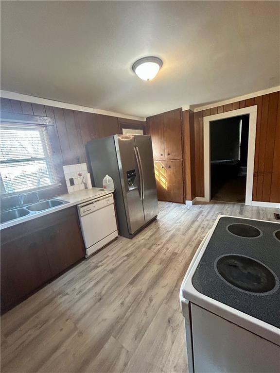 kitchen featuring wood walls, light countertops, light wood-style floors, white appliances, and a sink