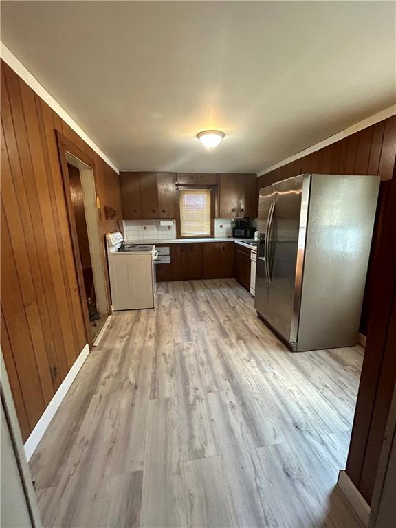 kitchen with white electric range, wooden walls, stainless steel fridge with ice dispenser, and light wood-type flooring