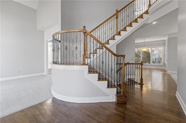 stairs featuring wood finished floors, baseboards, and a towering ceiling