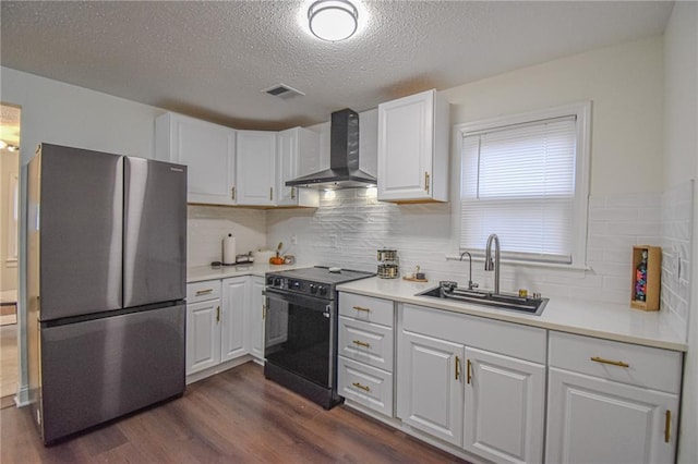 kitchen featuring visible vents, black electric range oven, a sink, freestanding refrigerator, and wall chimney exhaust hood