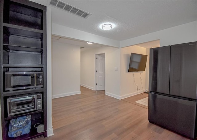 kitchen featuring wood finished floors, baseboards, visible vents, freestanding refrigerator, and a textured ceiling