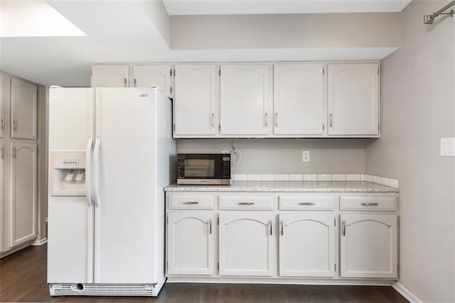 kitchen with white cabinets, dark wood-style floors, baseboards, and white fridge with ice dispenser