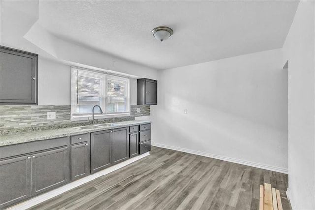 3309 E 69th St, Kansas City, MO 64132 - kitchen featuring gray cabinetry, baseboards, decorative backsplash, light wood-style flooring, and a sink