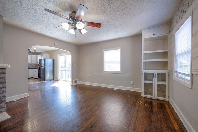 unfurnished living room featuring visible vents, dark wood-style floors, arched walkways, and a wealth of natural light