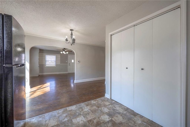 unfurnished dining area with a ceiling fan, baseboards, wood finished floors, arched walkways, and a textured ceiling