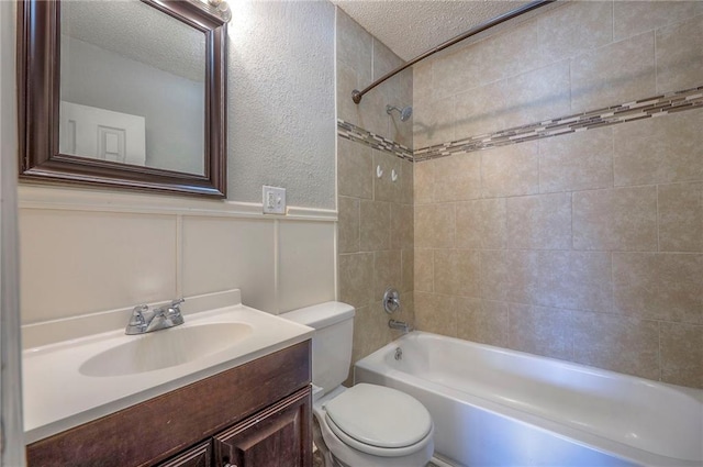 bathroom featuring a wainscoted wall, toilet, vanity, a textured ceiling, and  shower combination