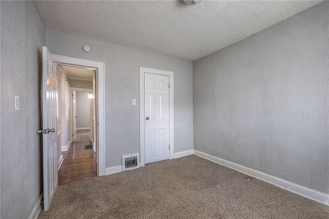 unfurnished bedroom with carpet flooring, a textured wall, visible vents, and a textured ceiling