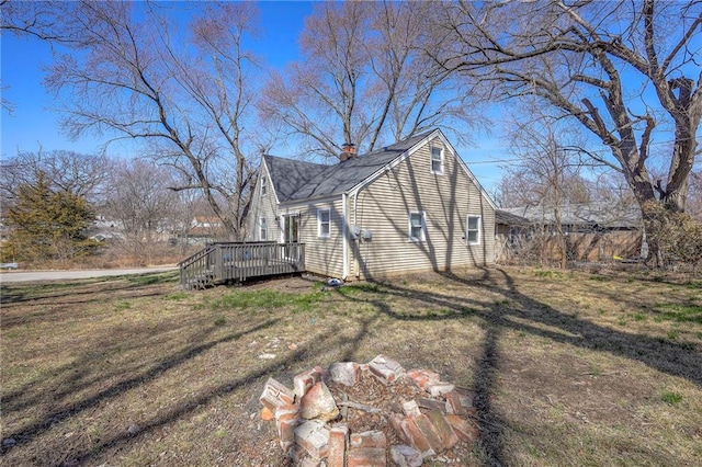 view of side of property featuring a wooden deck, a yard, a chimney, and a shingled roof