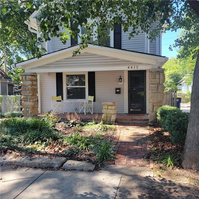 view of front of property with stone siding, covered porch, and fence