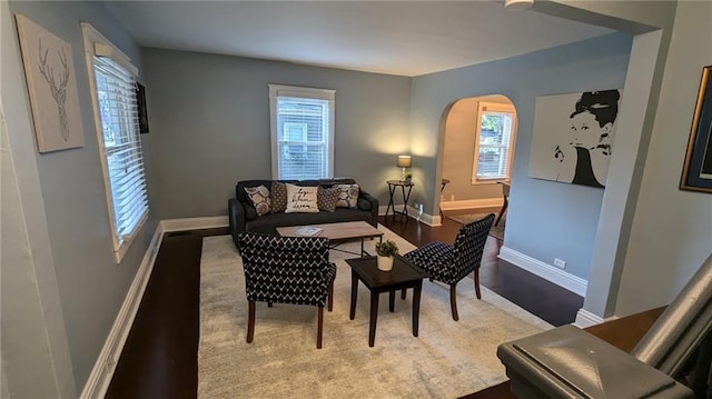 living area with arched walkways, baseboards, and wood finished floors