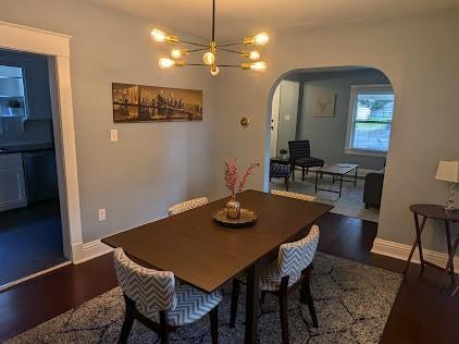 dining space with baseboards, arched walkways, an inviting chandelier, and wood finished floors