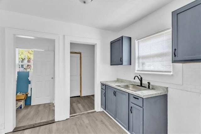 kitchen featuring gray cabinetry, light wood-style flooring, a sink, tasteful backsplash, and light countertops