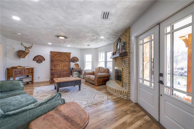 living area featuring recessed lighting, visible vents, a fireplace, and light wood finished floors