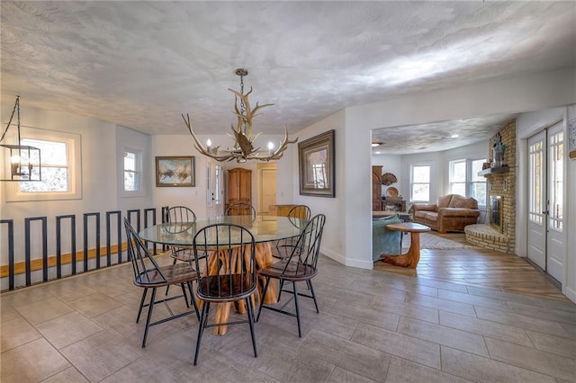 dining space featuring baseboards, a textured ceiling, a chandelier, and a fireplace