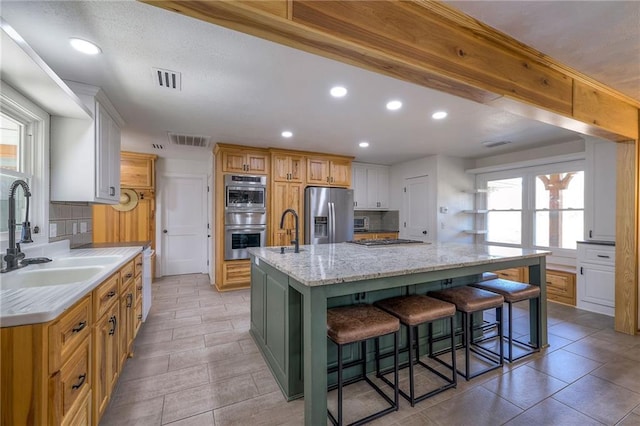 kitchen featuring visible vents, a large island with sink, a sink, appliances with stainless steel finishes, and tasteful backsplash