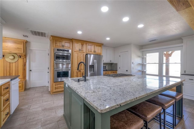 kitchen with light stone countertops, visible vents, a sink, stainless steel appliances, and a large island