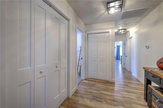 hall with baseboards, visible vents, and light wood-type flooring