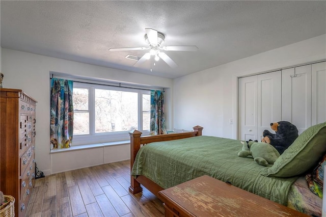 bedroom featuring visible vents, a ceiling fan, a textured ceiling, wood finished floors, and a closet