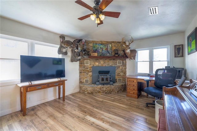 office space featuring wood finished floors, baseboards, visible vents, a wood stove, and ceiling fan