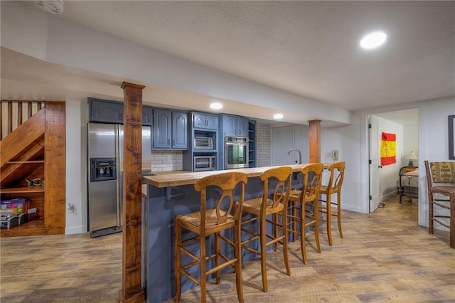 kitchen with wood finished floors, a breakfast bar, blue cabinetry, appliances with stainless steel finishes, and butcher block counters