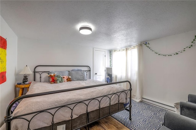 bedroom with wood finished floors, baseboard heating, and a textured ceiling