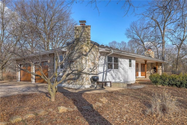 exterior space with stone siding, covered porch, concrete driveway, and a chimney