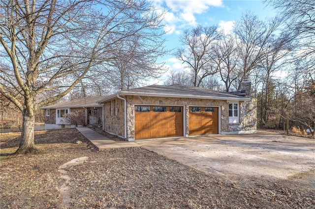 view of front of home featuring a garage, stone siding, concrete driveway, and a chimney