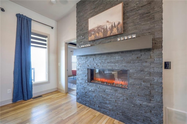 unfurnished living room featuring visible vents, a fireplace, baseboards, and wood finished floors