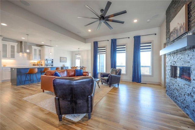 living room with a wealth of natural light, light wood-style floors, a stone fireplace, and ceiling fan