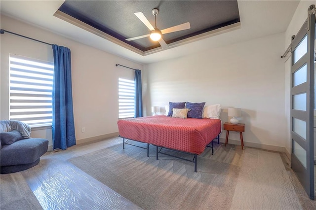 bedroom with a barn door, multiple windows, a raised ceiling, and baseboards